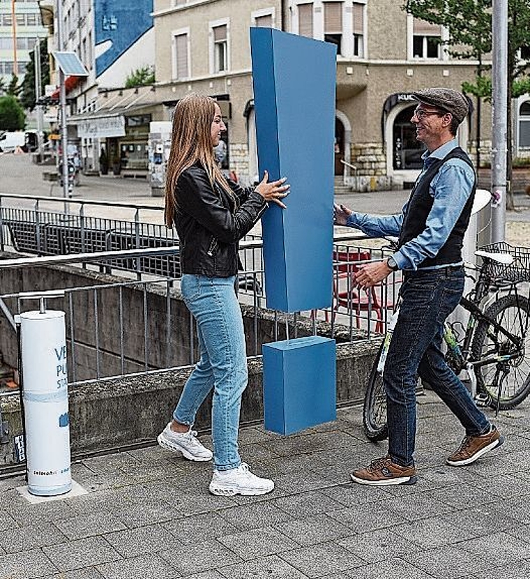 Die Grenchner Leichtathletin Lenja Heusser übergibt symbolisch das blaue Ausrufezeichen an Sacha Nussbaumer, Präsident Smart City Lab Grenchen. Er macht sich weiter und sieht auf dem Weg zum Südbahnhof das Plakat vom Repair-Café. Links zu erkenne